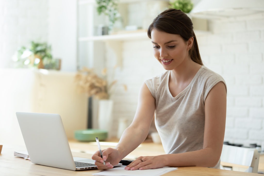 A woman reviewing paperwork with a laptop and calculator at her desk