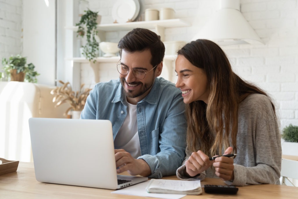 A smiling couple reviewing bills and finances together on a laptop at home