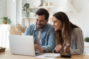 A smiling couple reviewing bills and finances together on a laptop at home