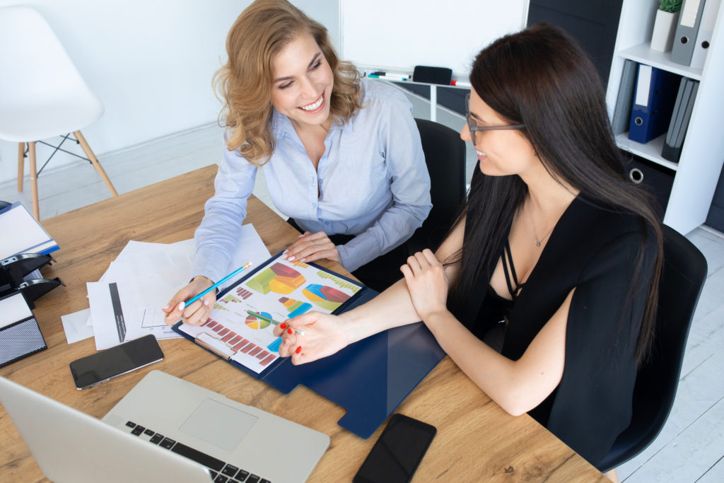 Two businesswomen reviewing a colorful financial report and charts together at a desk