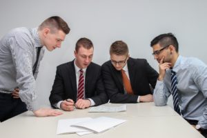 Four business professionals in suits reviewing a document together at a table